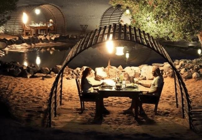 Couple dining under an illuminated canopy by the water at night