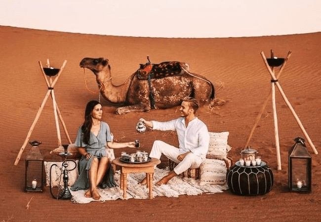 Romantic desert dinner on cushions with lanterns and a camel resting behind