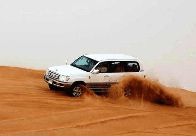 White SUV accelerating across a desert dune, sand spraying — desert safari