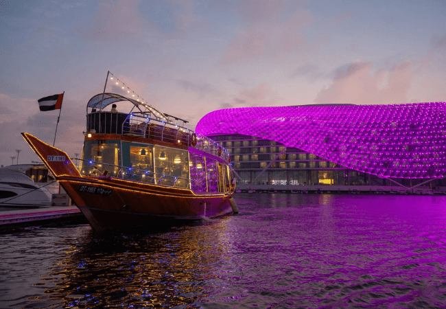 Illuminated dhow docked at Yas Marina, Abu Dhabi, beside the purple-lit hotel canopy at dusk